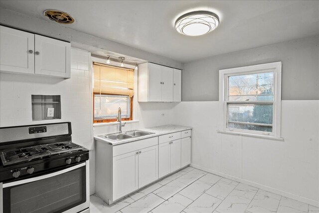 kitchen featuring stainless steel gas range, white cabinets, and sink