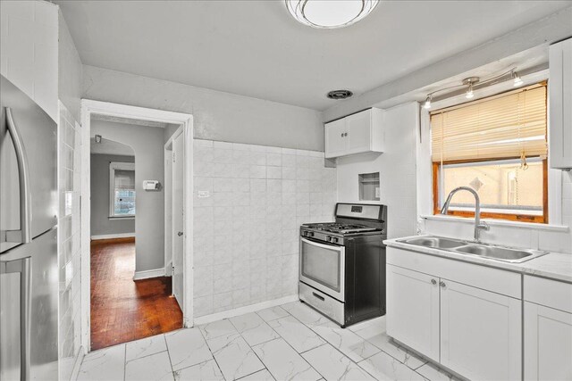 kitchen with appliances with stainless steel finishes, tile walls, light hardwood / wood-style floors, white cabinetry, and sink