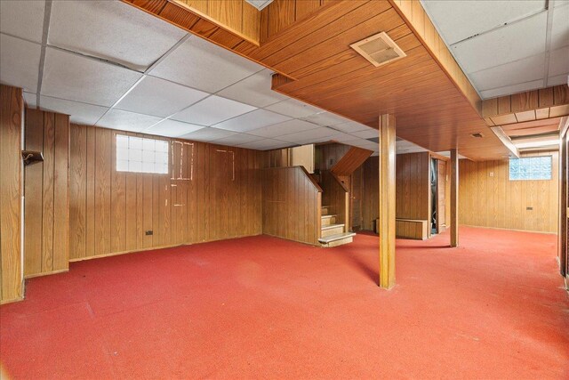 basement featuring light colored carpet, wood walls, and a healthy amount of sunlight