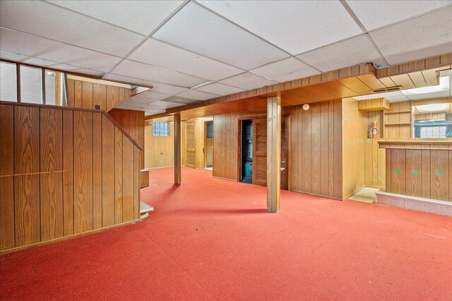 basement with wooden walls, carpet floors, a healthy amount of sunlight, and a paneled ceiling