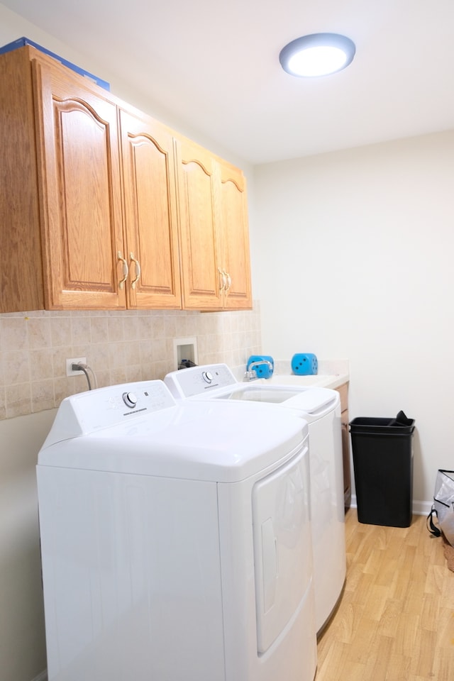 laundry area featuring light hardwood / wood-style flooring, washing machine and dryer, and cabinets