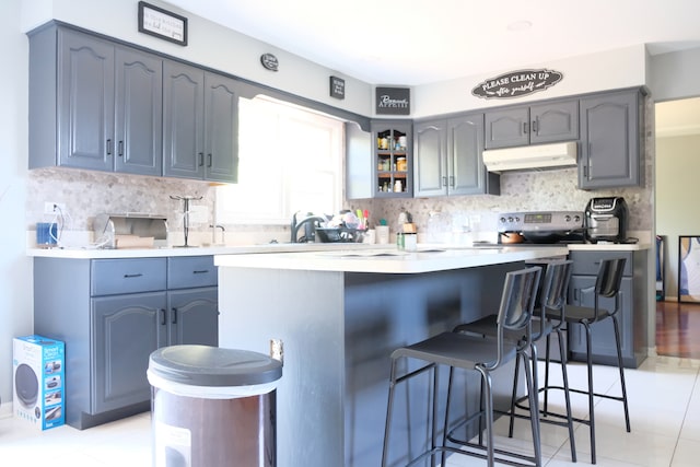 kitchen with decorative backsplash, kitchen peninsula, light tile patterned flooring, a kitchen bar, and electric stove