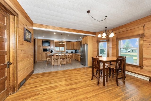 dining space with an inviting chandelier, baseboard heating, light hardwood / wood-style floors, and wood walls