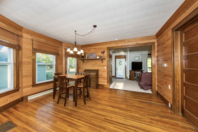 dining room with a healthy amount of sunlight, wood-type flooring, an inviting chandelier, and wood walls