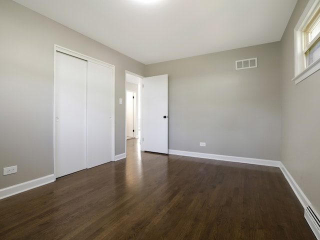 unfurnished bedroom featuring dark hardwood / wood-style floors, a baseboard radiator, and a closet