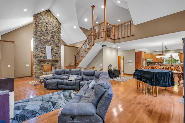 living room featuring high vaulted ceiling, a fireplace, a chandelier, and light hardwood / wood-style floors