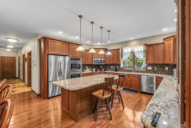 kitchen featuring light stone counters, a kitchen island, light hardwood / wood-style flooring, decorative light fixtures, and stainless steel appliances