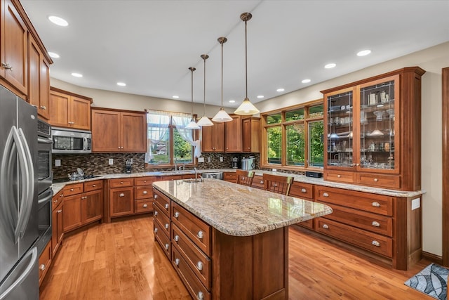 kitchen with a kitchen island with sink, pendant lighting, tasteful backsplash, light hardwood / wood-style flooring, and stainless steel appliances