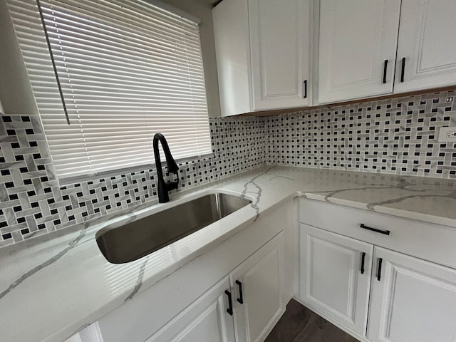 kitchen featuring light stone countertops, white cabinets, tasteful backsplash, and sink