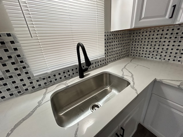 details with light stone counters, backsplash, sink, and white cabinetry