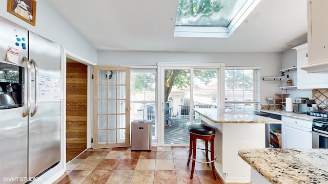 kitchen featuring light stone counters, a skylight, stainless steel appliances, and white cabinetry