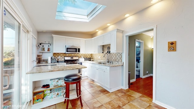 kitchen with white cabinets, sink, stainless steel appliances, light stone countertops, and decorative backsplash