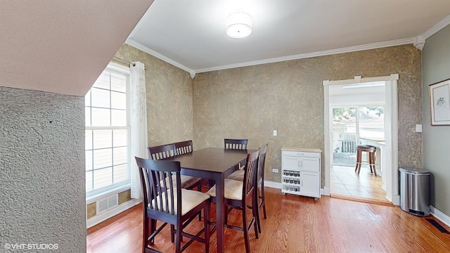 dining area featuring wood-type flooring, a healthy amount of sunlight, and crown molding