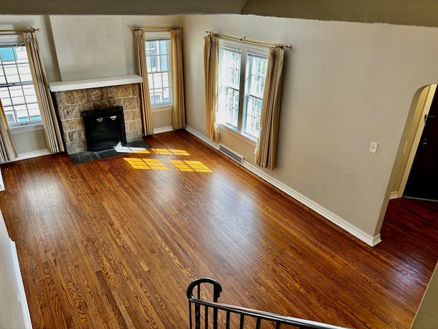 unfurnished living room featuring a tiled fireplace, vaulted ceiling, hardwood / wood-style flooring, and a healthy amount of sunlight