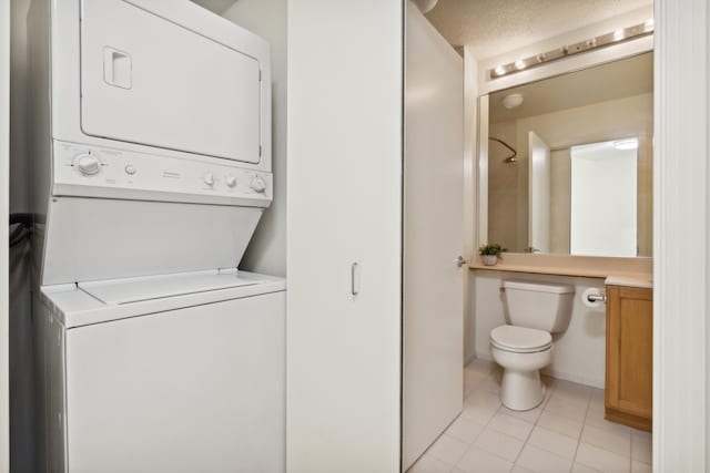 clothes washing area with a textured ceiling, stacked washing maching and dryer, and light tile patterned flooring