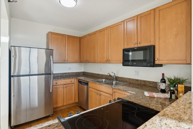 kitchen with light wood-type flooring, sink, stone counters, and stainless steel appliances