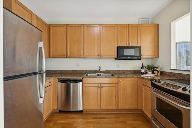 kitchen featuring light hardwood / wood-style floors, sink, stainless steel appliances, and dark stone counters