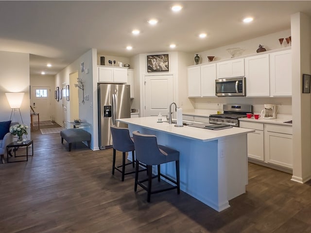 kitchen with appliances with stainless steel finishes, white cabinetry, dark wood-type flooring, and an island with sink