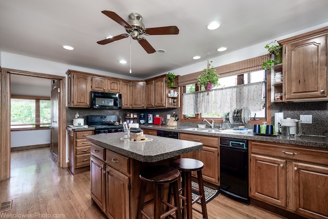 kitchen featuring decorative backsplash, black appliances, a center island, light hardwood / wood-style flooring, and sink