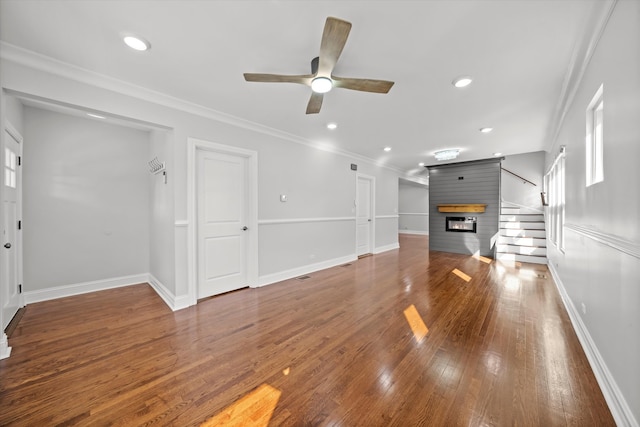 unfurnished living room featuring dark hardwood / wood-style floors, ornamental molding, a large fireplace, and ceiling fan