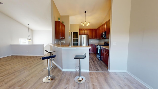 kitchen featuring a notable chandelier, kitchen peninsula, a kitchen breakfast bar, stainless steel appliances, and light hardwood / wood-style flooring