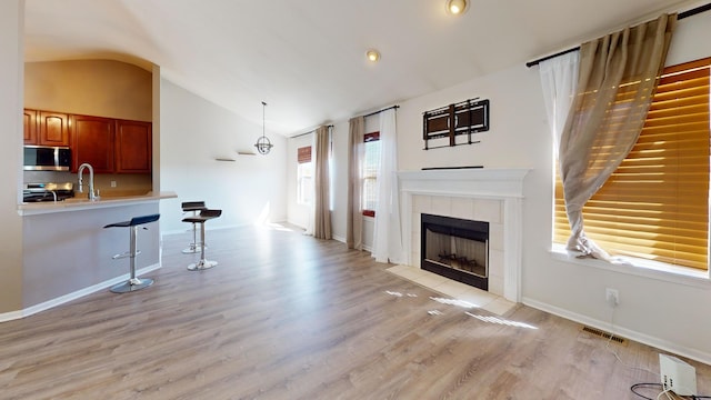 living room featuring light wood-type flooring, vaulted ceiling, a tiled fireplace, and sink