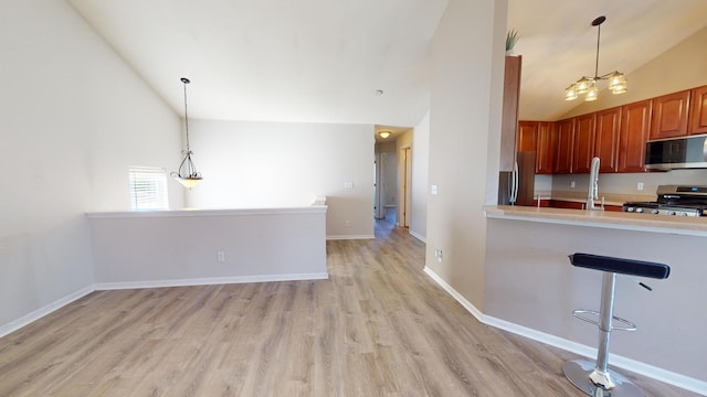 kitchen with high vaulted ceiling, stainless steel appliances, hanging light fixtures, and light wood-type flooring