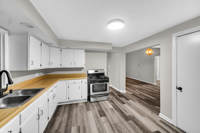 kitchen featuring wood-type flooring, stainless steel gas range, sink, and white cabinetry