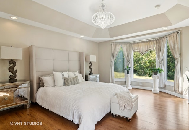 bedroom with a notable chandelier, a raised ceiling, and hardwood / wood-style floors