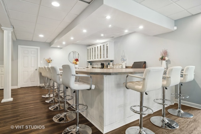 bar featuring a paneled ceiling, white cabinets, dark wood-type flooring, and ornate columns