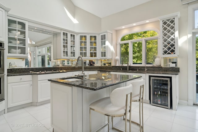 kitchen with light tile patterned flooring, white cabinets, beverage cooler, dark stone counters, and sink