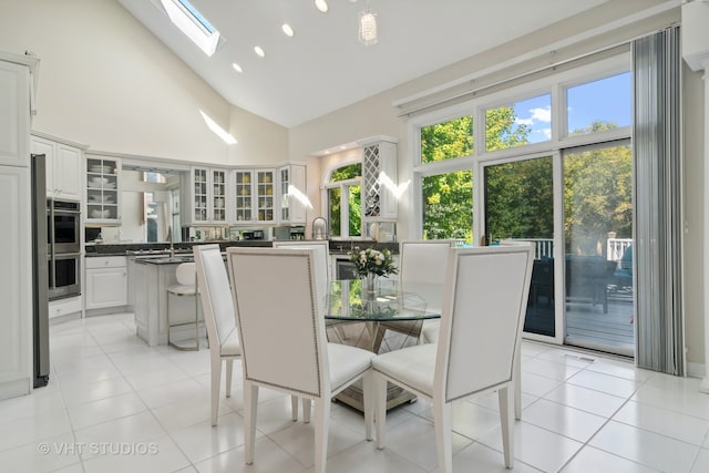 tiled dining room with high vaulted ceiling, a skylight, and sink