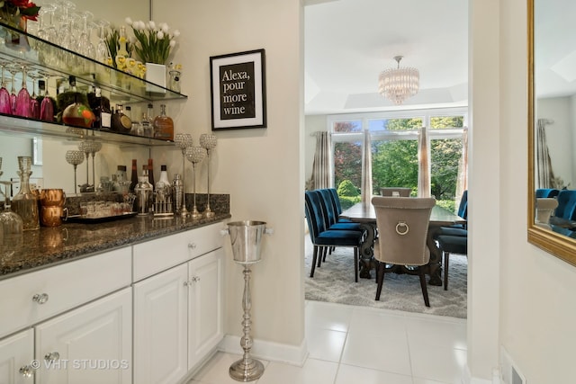 bar with dark stone countertops, white cabinetry, light tile patterned floors, an inviting chandelier, and decorative light fixtures