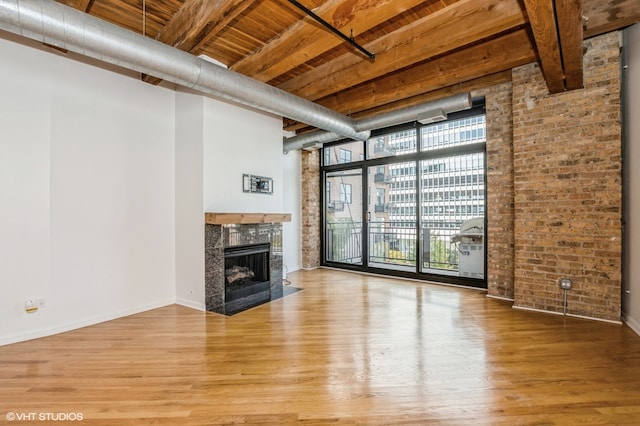 unfurnished living room with a wall of windows, brick wall, beamed ceiling, wooden ceiling, and hardwood / wood-style floors