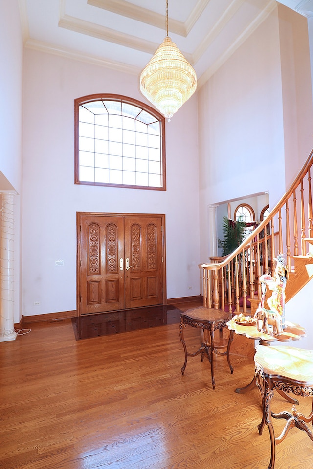 entrance foyer featuring an inviting chandelier, ornamental molding, hardwood / wood-style floors, and a towering ceiling