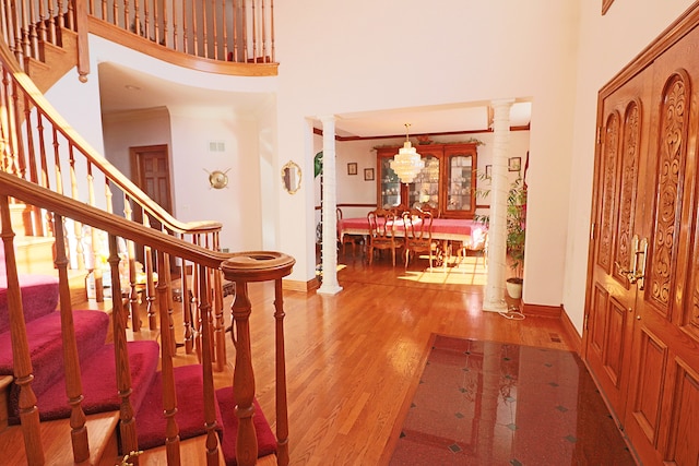 foyer with wood-type flooring, ornamental molding, a towering ceiling, and ornate columns