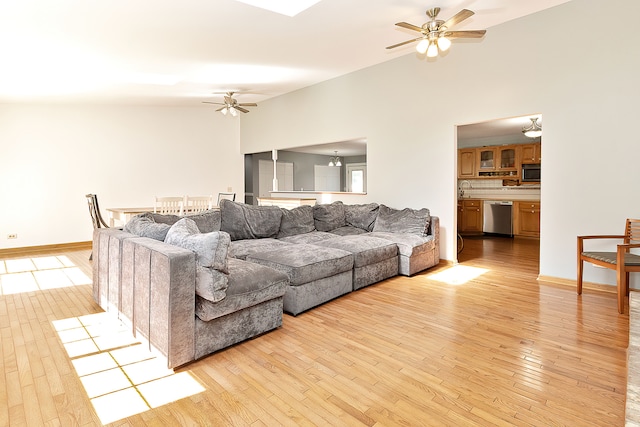 living room with light wood-type flooring, sink, ceiling fan, and high vaulted ceiling