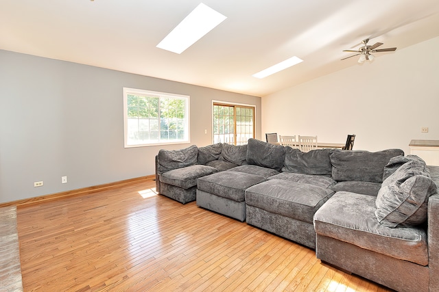 living room featuring vaulted ceiling with skylight, ceiling fan, and light wood-type flooring