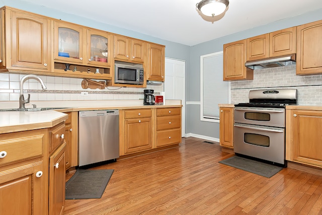 kitchen featuring decorative backsplash, stainless steel appliances, light wood-type flooring, sink, and extractor fan