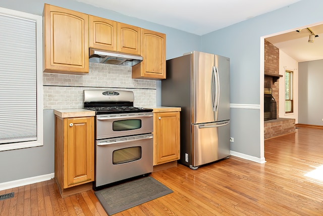 kitchen featuring stainless steel appliances, a fireplace, extractor fan, and light hardwood / wood-style flooring