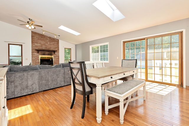 dining space featuring light wood-type flooring, vaulted ceiling with skylight, a fireplace, and ceiling fan