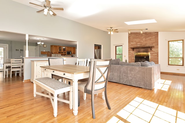 dining space featuring rail lighting, ceiling fan with notable chandelier, a fireplace, light wood-type flooring, and lofted ceiling