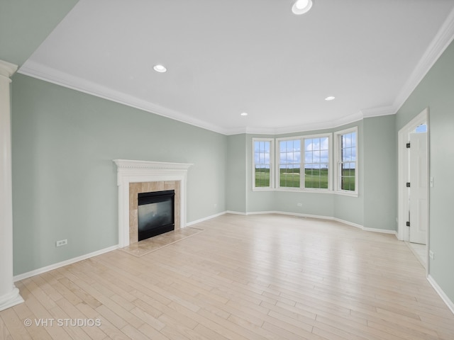 unfurnished living room with decorative columns, light hardwood / wood-style floors, ornamental molding, and a tiled fireplace