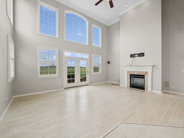 unfurnished living room featuring a fireplace, a towering ceiling, light wood-type flooring, and crown molding