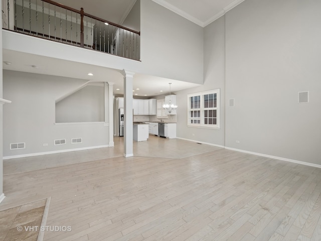 unfurnished living room with crown molding, light hardwood / wood-style flooring, ornate columns, a towering ceiling, and a notable chandelier