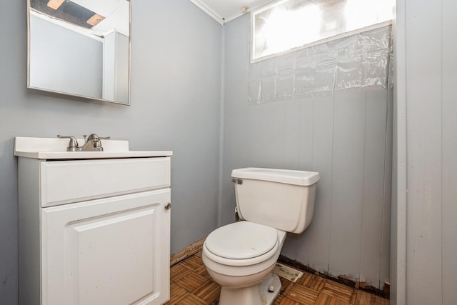 bathroom with parquet flooring, toilet, vanity, and ornamental molding