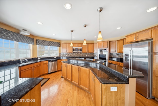 kitchen featuring light wood-type flooring, stainless steel appliances, decorative light fixtures, dark stone countertops, and a center island