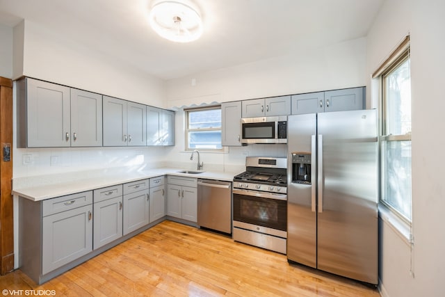 kitchen with sink, appliances with stainless steel finishes, light wood-type flooring, and a healthy amount of sunlight