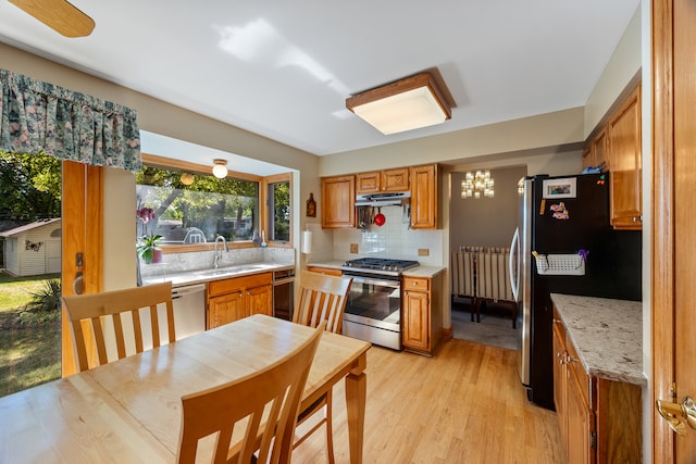 kitchen featuring decorative backsplash, light stone countertops, stainless steel appliances, sink, and light hardwood / wood-style flooring