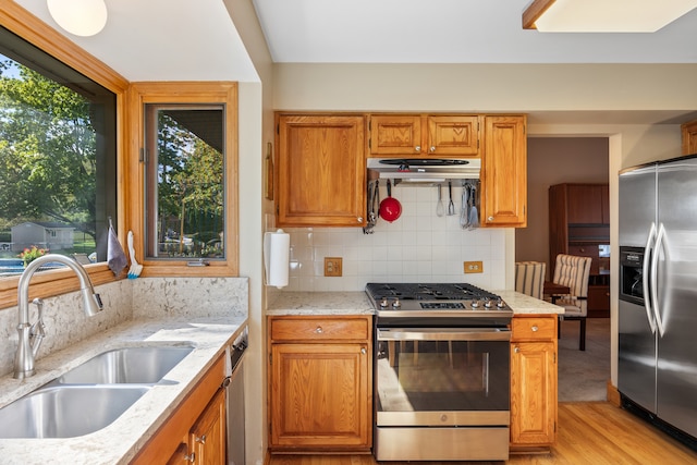 kitchen with light stone countertops, appliances with stainless steel finishes, light wood-type flooring, backsplash, and sink